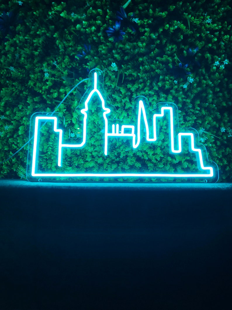 May include: A neon sign shaped like a city skyline, with a tall building in the center, against a green background.