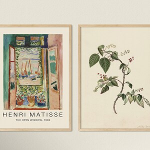 May include: Two framed art prints. The left print is a painting of a window with a view of boats and water. The text below the painting reads "Henri Matisse, The Open Window, 1905". The right print is a botanical illustration of a green plant with red berries.