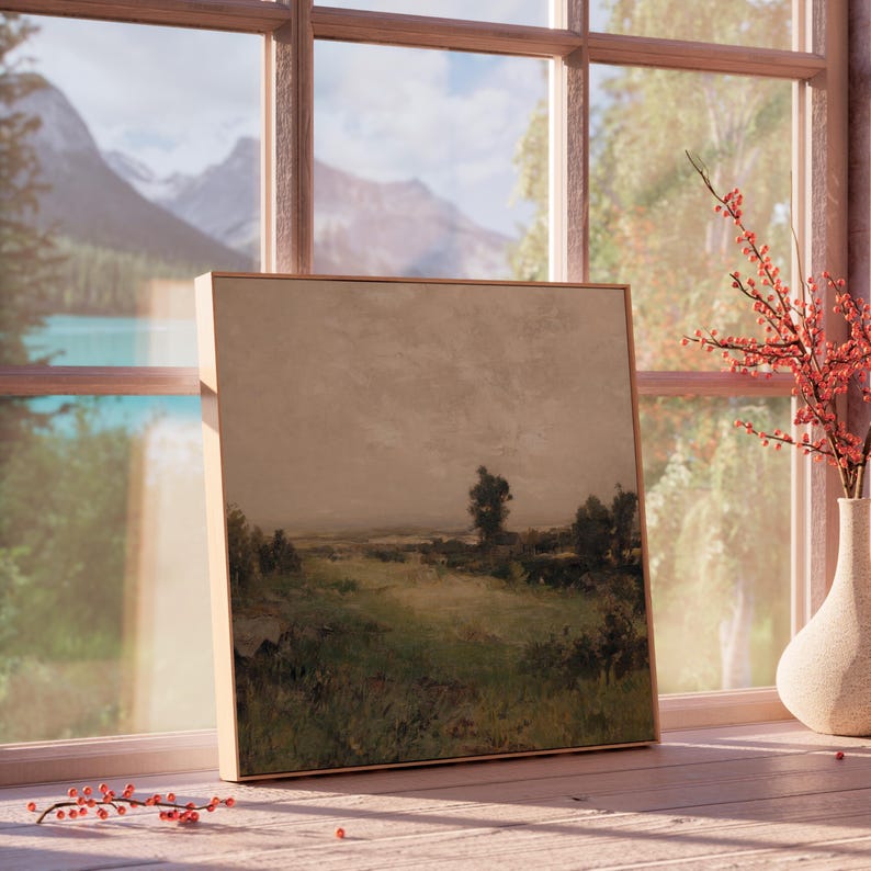 May include: A framed landscape painting with a muted color palette, featuring a field, trees, and a cloudy sky. The artwork is displayed on a wooden windowsill, with a vase of red berries and a scenic mountain view visible through the window.