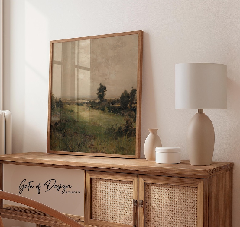 May include: A framed landscape art print with a wooden frame. The artwork depicts a field with green grass and trees under a cloudy sky. The print is displayed on a wooden cabinet with a lamp and decorative vases. The text "Gate of Design STUDIO" is visible.