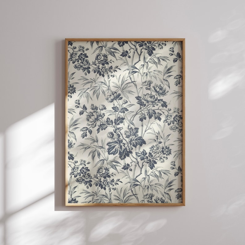 Op de afbeelding: Een ingelijste print met een gedetailleerd bloemenpatroon in blauw en wit. Het ontwerp bevat bloemen, bladeren en bamboestengels tegen een lichte achtergrond. De print is ingelijst in een natuurlijke houten lijst, voor een klassieke uitstraling.