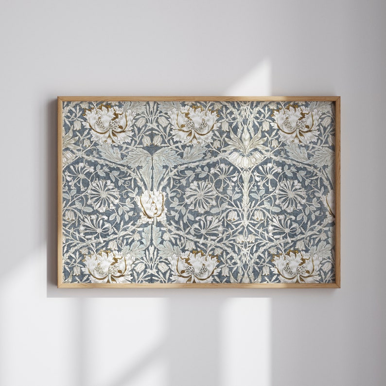Op de afbeelding: Een ingelijste print met een gedetailleerd bloemenpatroon in blauw, wit en goud. Het kunstwerk toont een ingewikkeld ontwerp van gestileerde bloemen en bladeren op een getextureerde achtergrond. De lijst is gemaakt van lichtgekleurd hout.