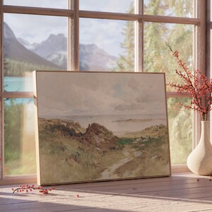 May include: A framed watercolor painting of a landscape with a path leading to a body of water. The painting is on a wooden table with a vase of red berries and a small ceramic vase.