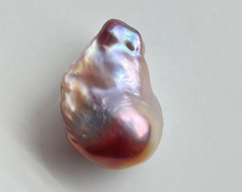 May include: A large, iridescent, baroque pearl with a pink, purple, and blue hue. The pearl has an irregular shape and a smooth surface.