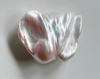 May include: A large, irregularly shaped, white pearl with iridescent highlights. The pearl has a smooth, glossy surface and a slightly pink hue.