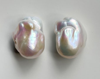 May include: Two large, irregular, white baroque pearls with iridescent sheen. The pearls are smooth and have a slightly off-white color.