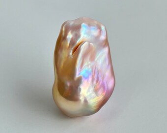 May include: A large, irregularly shaped, iridescent pearl with a pink hue. The pearl has a smooth, glossy surface and displays a rainbow of colors.