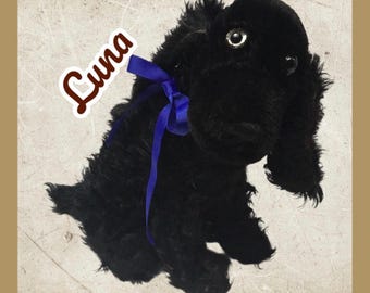 以下が含まれることがあります： 青いリボンが首に巻かれた黒い犬のぬいぐるみ。 大きな垂れ耳とふわふわの毛並みが特徴です。 「Luna」の文字が筆記体で書かれたステッカーが付いています。