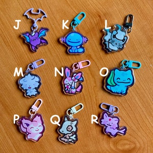May include: Nine colorful keychains featuring cartoon characters from popular video games and anime. Each keychain has a different character and is made of clear acrylic. The keychains are arranged in a grid pattern on a wooden surface.