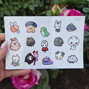 Könnte beinhalten: Ein Bogen mit Aufklebern mit verschiedenen Cartoon-Charakteren. Die Aufkleber zeigen eine Vielzahl farbenfroher Designs, wie z. B. eine Biene mit einer Blume, ein Pilz-Kreatur und einen grünen Dinosaurier. Die Aufkleber befinden sich auf weißem Hintergrund.