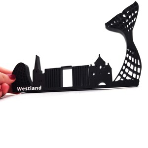 May include: Black silhouette of a city skyline with the word "Westland" printed below. The skyline includes a tall, thin building, a building with a dome, and a large, curved structure.