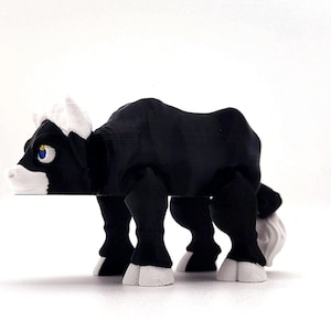 May include: A black and white bull figurine with a white face and horns. The bull has a blue eye and is standing on a white surface.