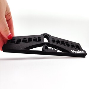 May include: Black foam cutout of the Rialto Bridge in Venice, Italy. The bridge is arched and has a gondola underneath. The word "Venice" is printed in white on the right side of the cutout.