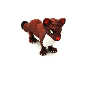May include: A brown weasel figurine with a white chest and belly, red nose and ears, and a black-tipped tail. The weasel has yellow eyes and is standing on all fours. The figurine is set against a white background.