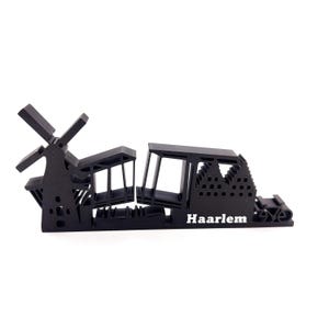 May include: Black silhouette of a windmill, a building, and a cityscape with the word "Haarlem" printed below.