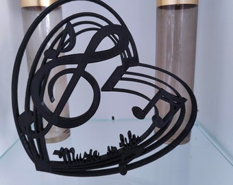 May include: Black metal heart-shaped music note design with the word "Music" written on the bottom. The design is sitting on a glass shelf with two clear glass bottles with gold tops.
