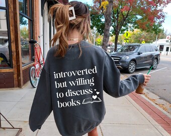 May include: A gray sweatshirt with the text "introverted but willing to discuss books" and a small illustration of an open book with two hearts.