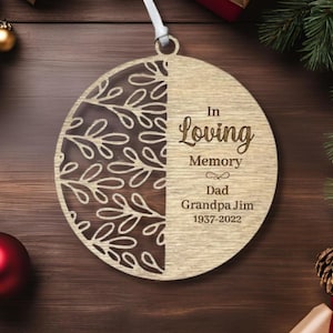 May include: A wooden Christmas bauble with a leafy design on one side and the text "In Loving Memory Dad Grandpa Jim 1937-2022" on the other side.