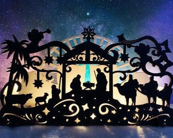 May include: A black silhouette of a nativity scene with a star above the stable. The scene includes a palm tree, a donkey, a camel, and three wise men. The background is a dark blue with white stars.