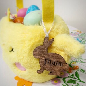 May include: A yellow chick Easter basket with a wooden bunny tag that says "Maia". The basket is filled with colourful Easter eggs.
