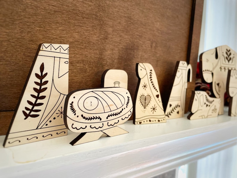 Pode incluir: Um conjunto de figuras de pres&eacute;pio de Natal em madeira, incluindo Maria, Jos&eacute;, o menino Jesus, um pastor, um burro e uma vaca. As figuras s&atilde;o pintadas em um estilo de arte popular simples com contornos pretos e detalhes brancos.