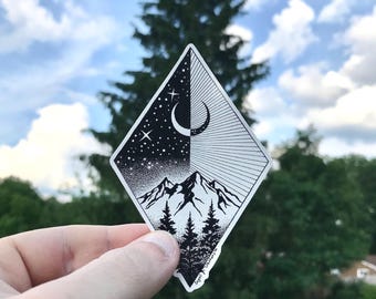 May include: A diamond-shaped sticker featuring a black and white illustration of a mountain range and pine trees. The upper half shows a crescent moon and stars on one side and radiating sunburst lines on the other, creating a day and night contrast.