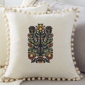 May include: Two white throw pillows with pom-pom trim. The front pillow features an embroidered design of a stylised tree with flowers and birds in shades of green, yellow, orange, and black.