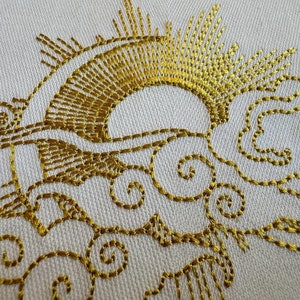 Puede incluir: Bordado dorado sobre tela blanca que representa un sol con rayos y nubes. El sol es un semicírculo con rayos que emanan de la parte superior. Las nubes son estilizadas y tienen un patrón de espiral.