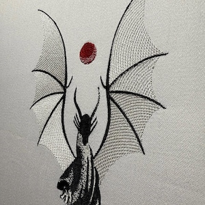 May include: Black embroidered dragon with outstretched wings, facing forward, against a white background. A red circle is above the dragon.