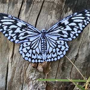 May include: A white and black butterfly embroidery patch with a light blue background. The butterfly is in a flying position with its wings spread out.