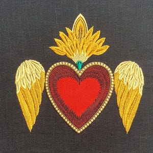 Puede incluir: Corazón bordado con alas y un halo dorado, un símbolo religioso tradicional. El corazón es rojo, las alas son doradas y el halo es dorado con un centro verde.