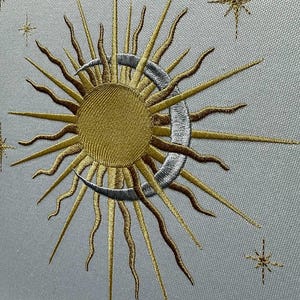 K&ouml;nnte beinhalten: Gestickte Darstellung einer Sonne und eines Mondes mit einer Sichelmondform. Die Sonne ist golden und der Mond ist silbern. Im Hintergrund befinden sich kleine Sterne.