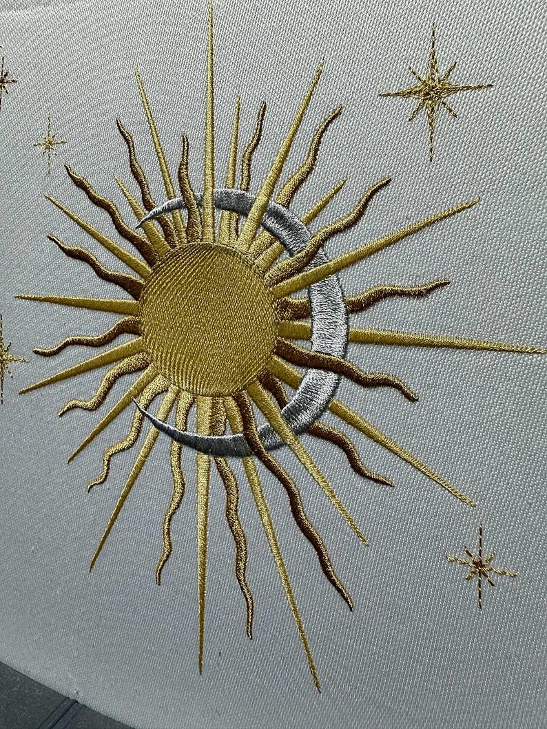 K&ouml;nnte beinhalten: Gestickte Darstellung einer Sonne und eines Mondes mit einer Sichelmondform. Die Sonne ist golden und der Mond ist silbern. Im Hintergrund befinden sich kleine Sterne.