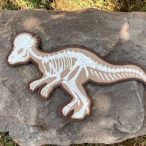 Iron on patch with a print of a famous dinosaur Pachycephalosaurus with bones which are glowing in the dark 7.5” x 4.5”
