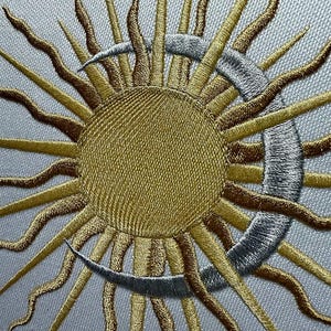 K&ouml;nnte beinhalten: Gestickte Sonnen- und Mond-Darstellung mit gold- und silberfarbenem Garn. Die Sonne hat eine gro&szlig;e, runde Mitte und viele Strahlen. Der Mond ist halbmondf&ouml;rmig.