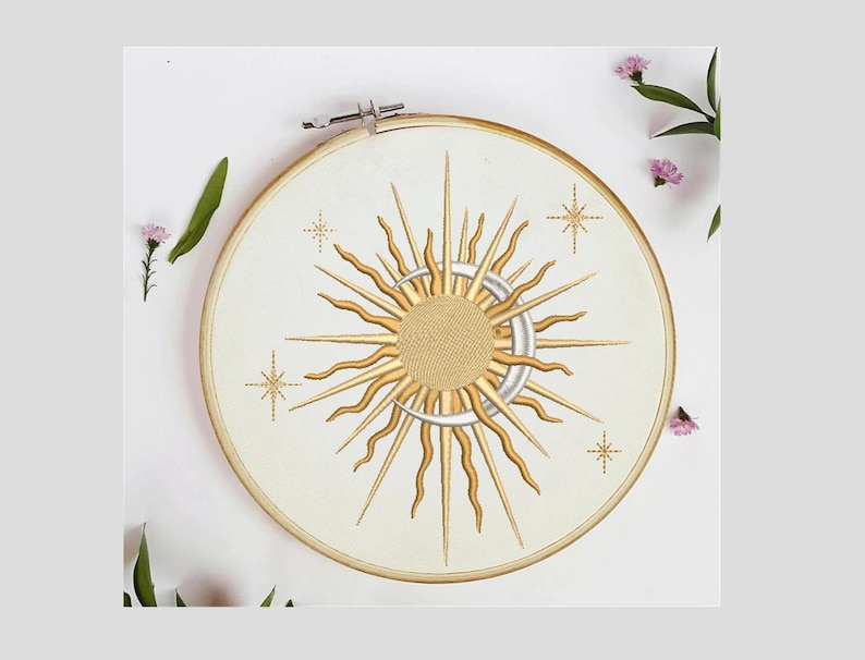 K&ouml;nnte beinhalten: Ein wei&szlig;er Stickrahmen mit einem goldenen Sonnen- und Mondmotiv. Die Sonne hat eine strukturierte Mitte und ist von Strahlen umgeben. Der Mond ist halbmondf&ouml;rmig. Um Sonne und Mond befinden sich vier kleine goldene Sterne.