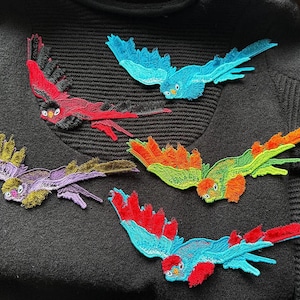 以下が含まれることがあります： 赤、青、緑、オレンジ、紫など、さまざまな色の鳥の刺繍パッチ。パッチは黒いセーターに適用されています。鳥は詳細な翼と顔の特徴を持っています。