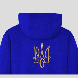 Puede incluir: Una sudadera con capucha azul con un tridente ucraniano bordado en oro en la espalda.