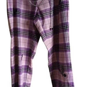 Op de afbeelding: Paarse geruite broek met een zilveren kettingriem. De broek heeft een rechte pijp en zwarte vleermuisafbeeldingen. Het ruitpatroon bevat tinten paars, zwart en wit.