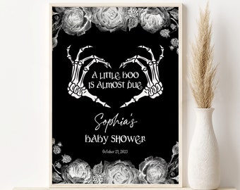 May include: Black and white printable baby shower invitation with a skeleton hand heart shape and the text "A little boo is almost due."  The invitation also includes the text "Sophia's Baby Shower" and the date "October 21, 2023".