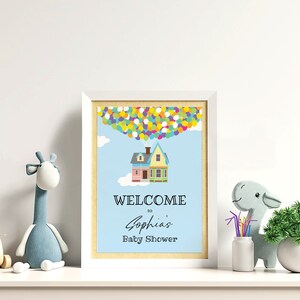 K&ouml;nnte beinhalten: Ein wei&szlig;er Rahmen mit blauem Hintergrund und einem Haus mit Ballons. Der Text lautet "Willkommen zur Babyparty von Sophia".