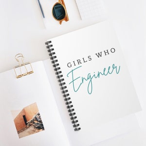 May include: A white spiral bound notebook with the text "GIRLS WHO ENGINEER" in black lettering and the word "Engineer" written in teal cursive.