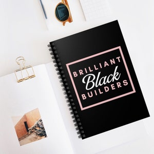 May include: A black spiral notebook with the text "BRILLIANT Black BUILDERS" in a pink square.