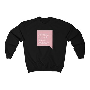 Puede incluir: Sudadera negra con un bocadillo rosa que contiene el texto "Actually, I do look like an engineer" en blanco. La sudadera es de cuello redondo.