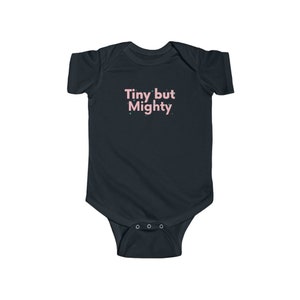 Könnte beinhalten: Ein dunkelblauer Baby Strampler mit dem Text "Tiny but Mighty" in rosa Schrift.