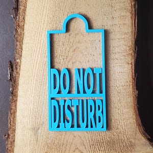 May include: A bright cyan door hanger featuring a rectangular frame with a rounded top hook. The cutout text reads DO NOT DISTURB in bold, capital letters, with the words stacked in two separate sections within the frame structure.