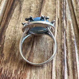 May include: A silver ring with a blue oval gemstone surrounded by silver flower accents.