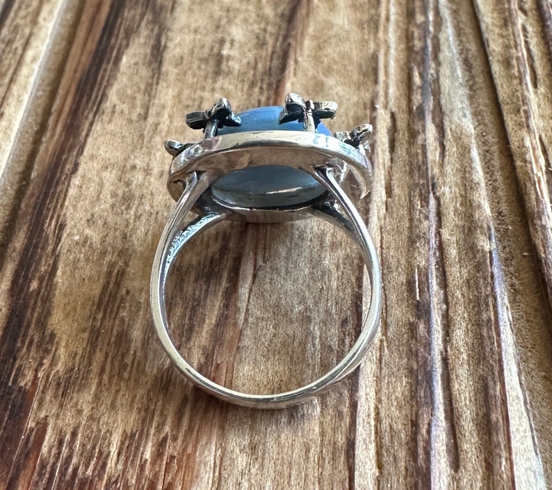 May include: A silver ring with a blue oval gemstone surrounded by silver flower accents.