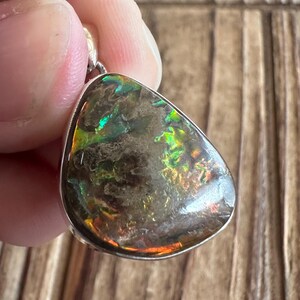 May include: A silver pendant with a teardrop-shaped iridescent gemstone. The gemstone has a dark brown base with flashes of green, blue, and orange.