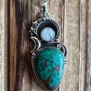 May include: A silver pendant with a green turquoise stone and a moonstone. The pendant is set in a silver frame with a crescent moon design and stars.